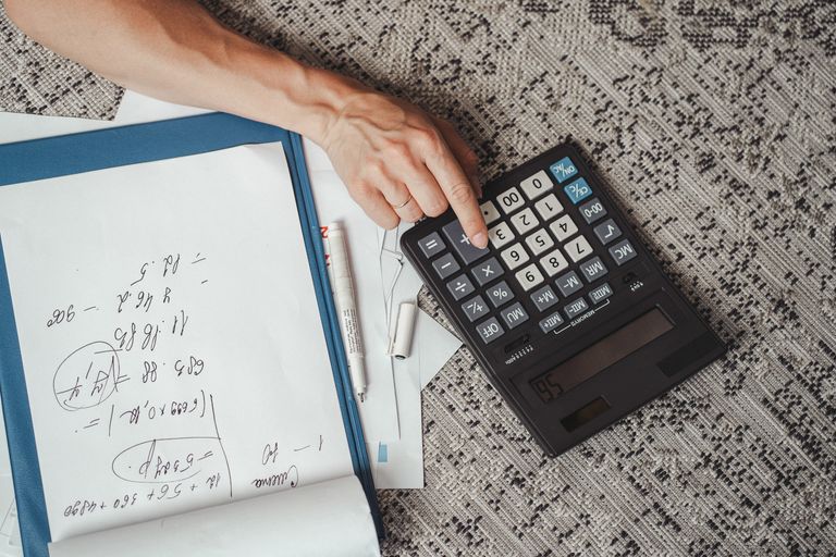 Mão usando uma calculadora ao lado de anotações sobre uma mesa.